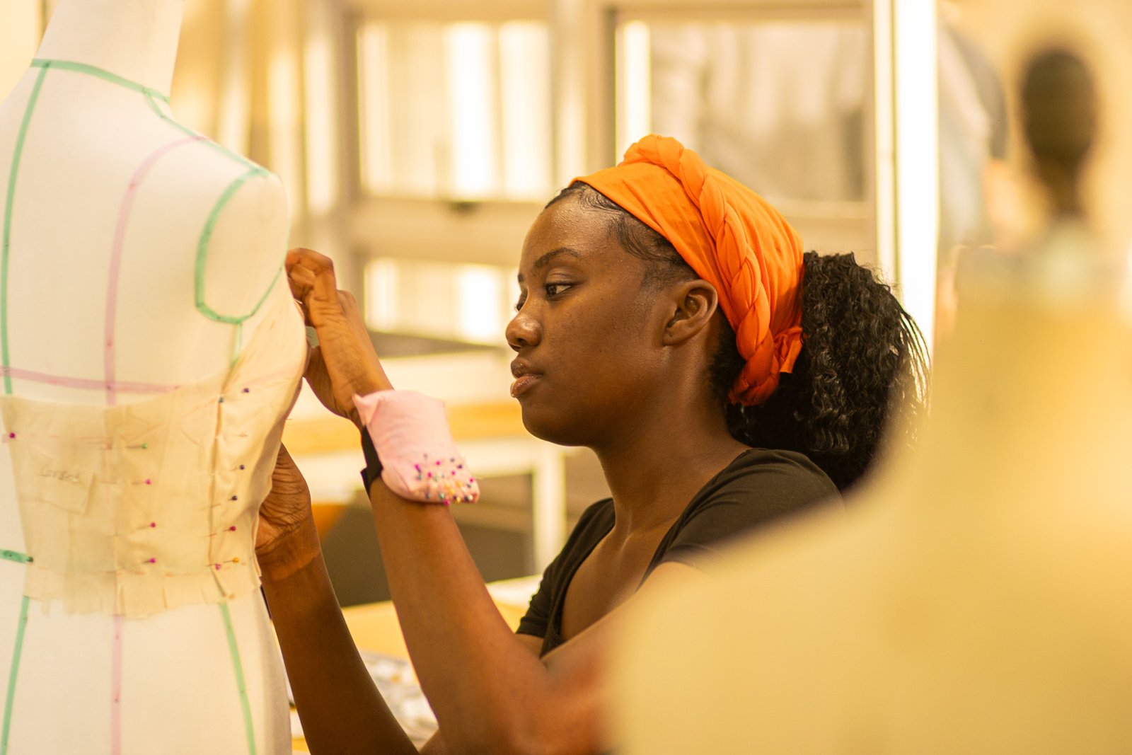 female in an orange headband pinning fabric to a mannequin